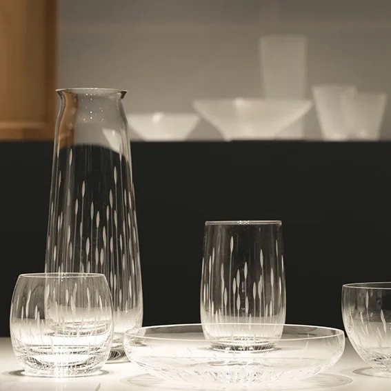 Carafe filled with water beside tumblers and a shallow glass bowl on a dark, moody table