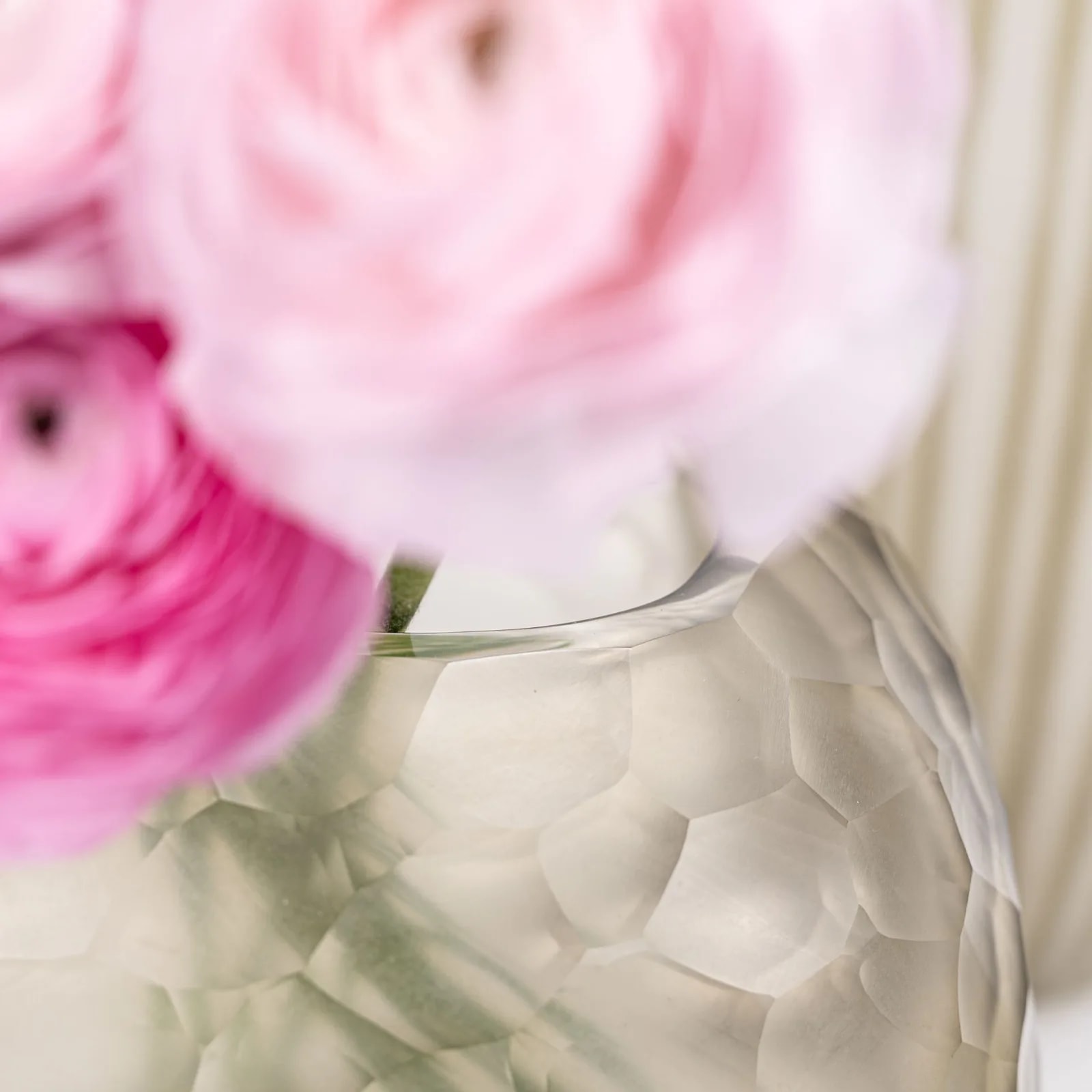 Detail of the frosted cut glass vase rim with pink ranunculus blooms above