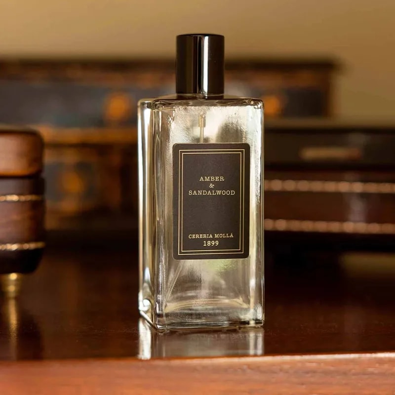 The Amber and Sandalwood glass bottle on a dark wood dresser with antique boxes softly blurred behind