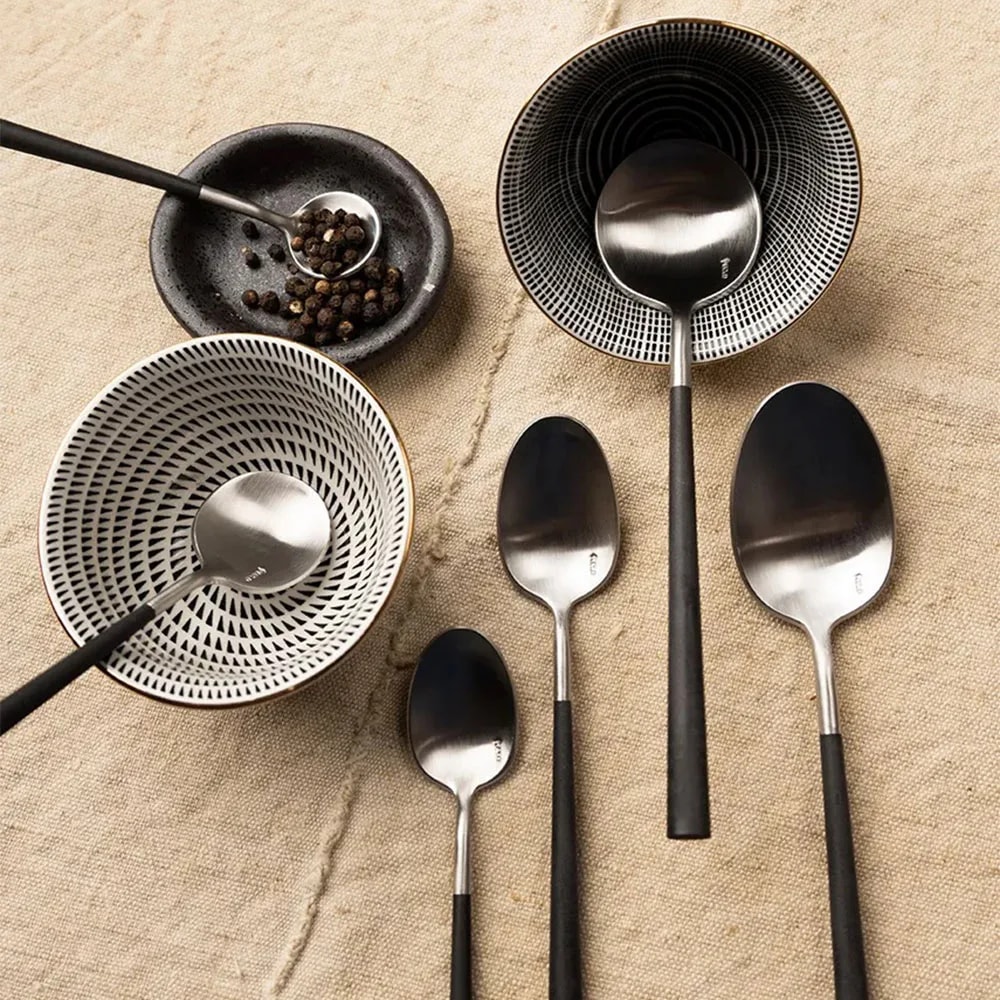 Overhead view of four Neo Black spoon sizes on linen beside patterned bowls and a dish of peppercorns
