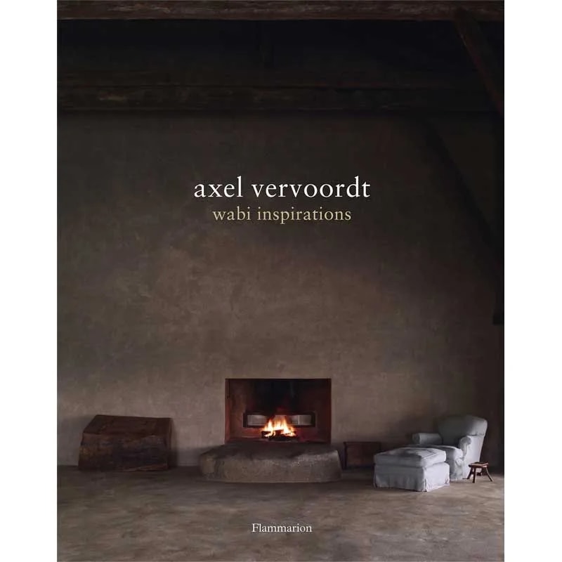 Wabi Inspirations hardcover cover with a dim plaster room, lit fireplace and pale slipcovered armchair
