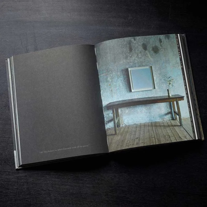 Wabi Inspirations open on a dark table: blank grey page and a rustic table below a framed panel