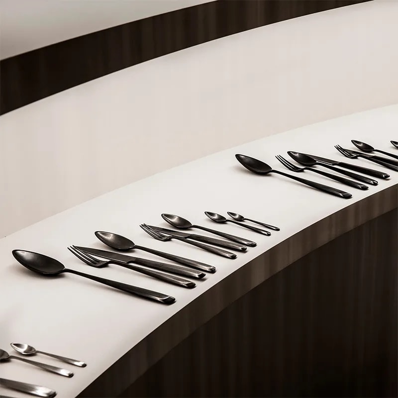 Zoë matt steel cutlery including the dessert spoon, lined up along a curved white display shelf